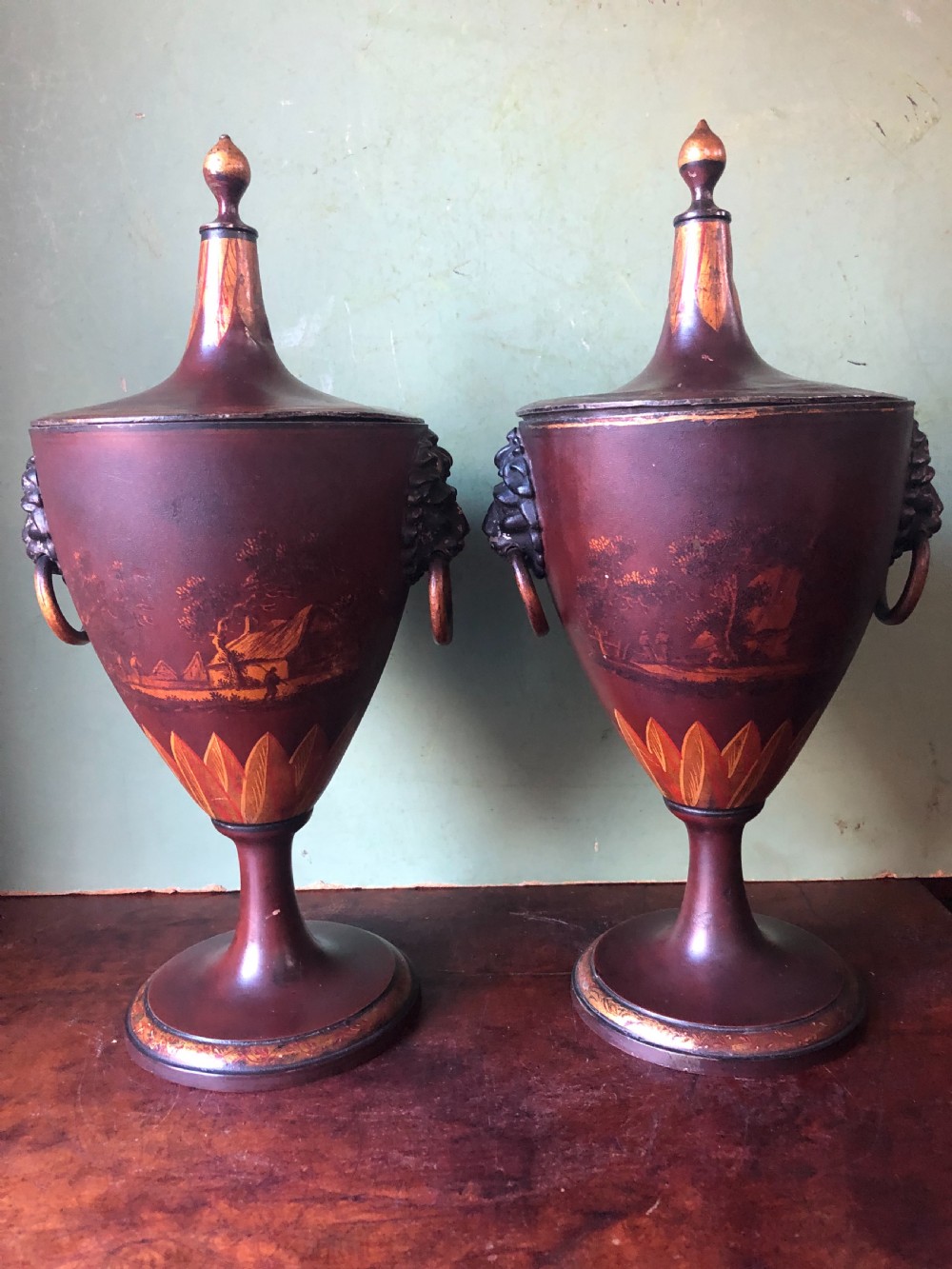 A pair of early 19th-century Dutch neoclassical chestnut urns in dark brown japanned pewter, painted with landscape scenes, leaf motifs, side ring handles, and tall finial lids. View III