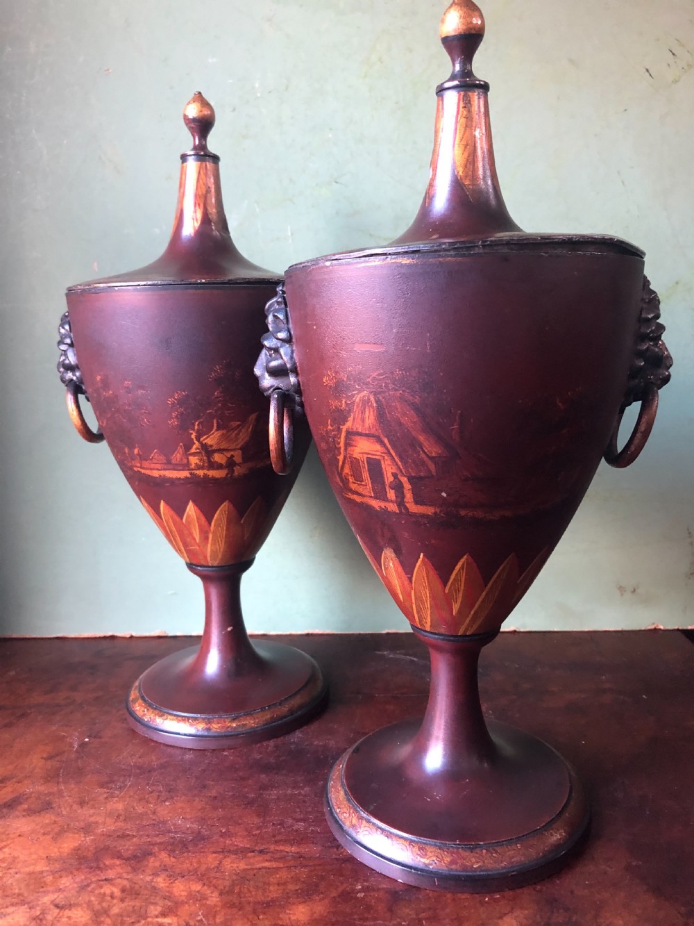 A pair of early 19th-century Dutch neoclassical chestnut urns in dark brown japanned pewter, painted with landscape scenes, leaf motifs, side ring handles, and tall finial lids. View VII