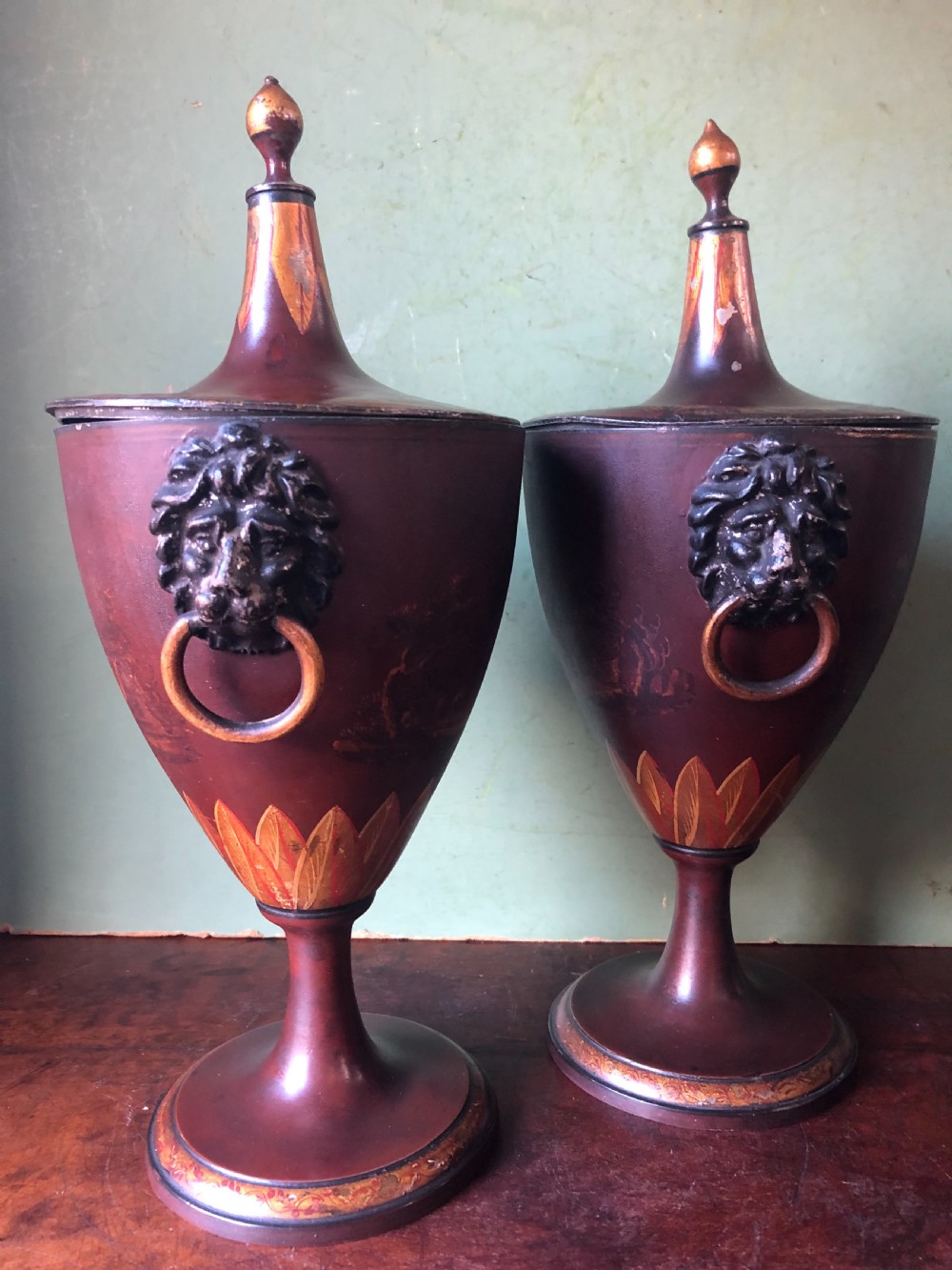 A pair of early 19th-century Dutch neoclassical chestnut urns in dark brown japanned pewter, painted with landscape scenes, leaf motifs, side ring handles, and tall finial lids. View IX