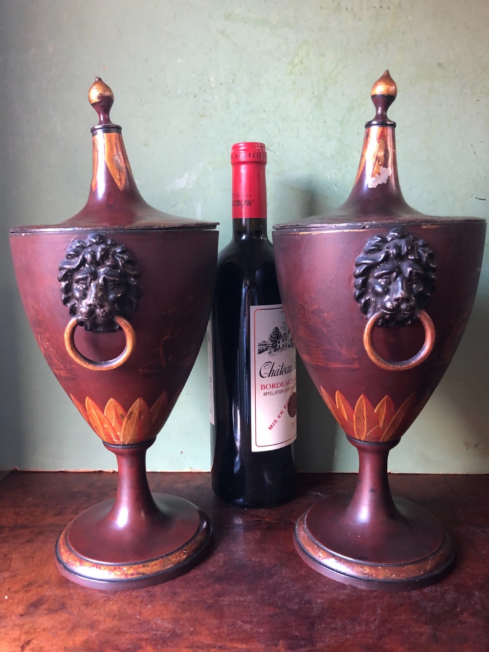 A pair of early 19th-century Dutch neoclassical chestnut urns in dark brown japanned pewter, painted with landscape scenes, leaf motifs, side ring handles, and tall finial lids. View X