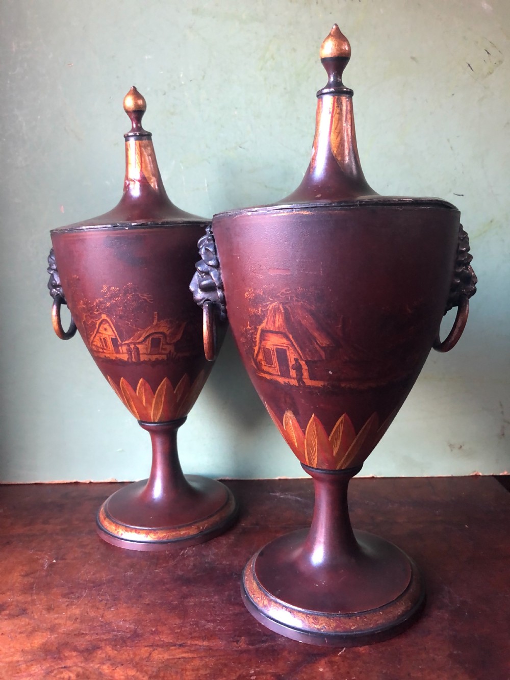 A pair of early 19th-century Dutch neoclassical chestnut urns in dark brown japanned pewter, painted with landscape scenes, leaf motifs, side ring handles, and tall finial lids. View XI