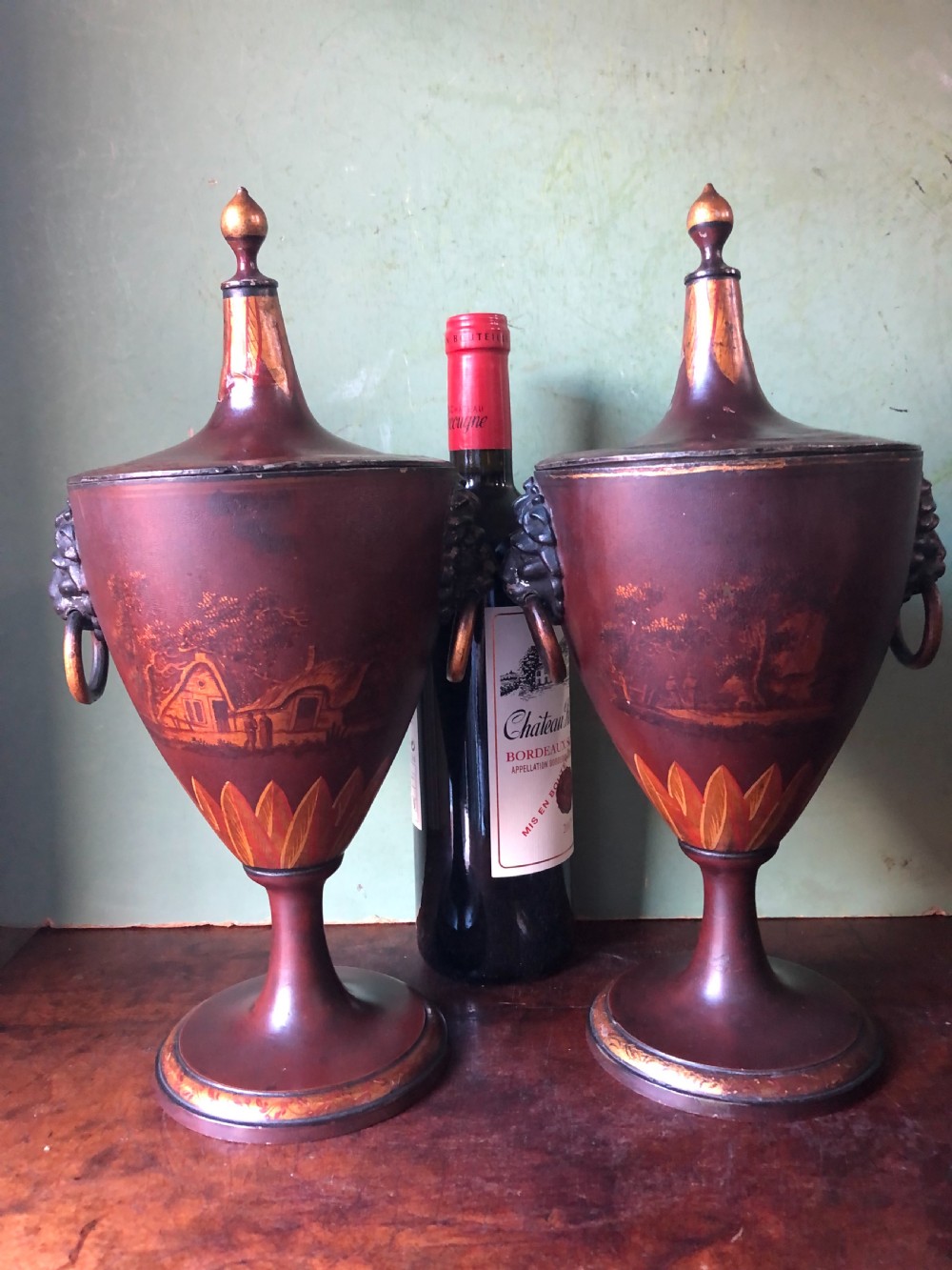 A pair of early 19th-century Dutch neoclassical chestnut urns in dark brown japanned pewter, painted with landscape scenes, leaf motifs, side ring handles, and tall finial lids. View XII