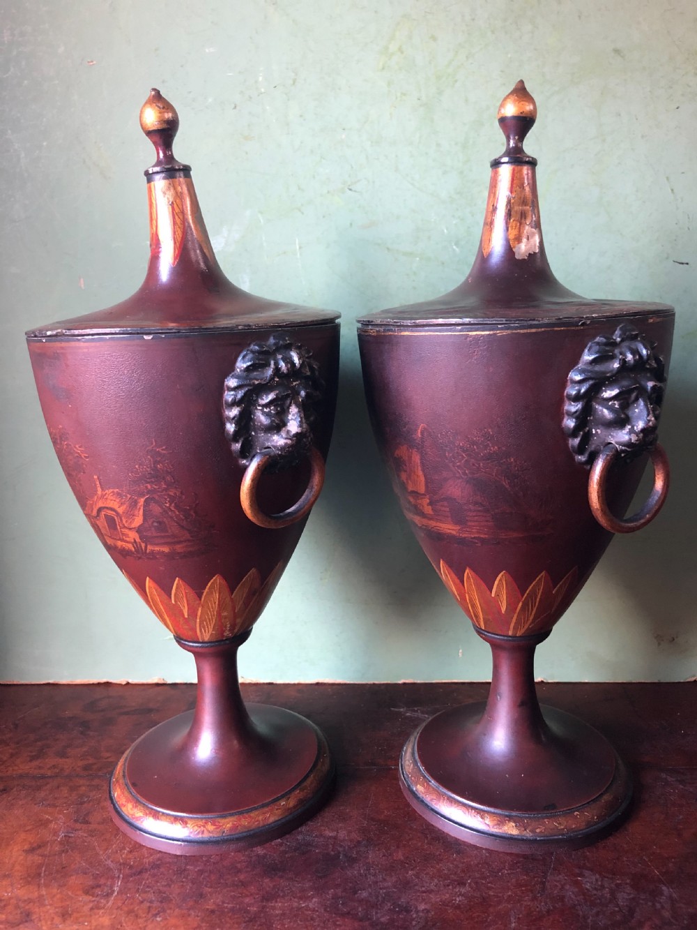 A pair of early 19th-century Dutch neoclassical chestnut urns in dark brown japanned pewter, painted with landscape scenes, leaf motifs, side ring handles, and tall finial lids. View XIII