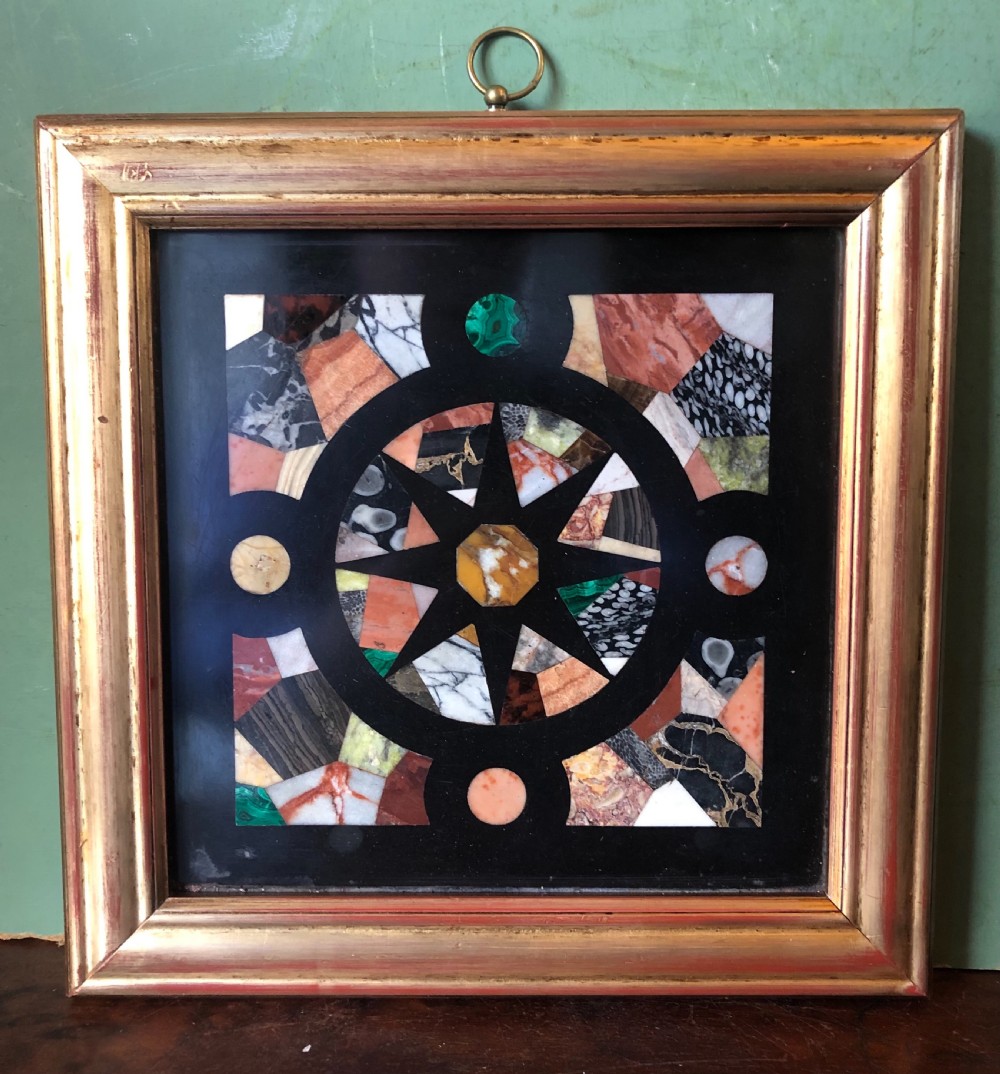 A square 19th-century Ashford black marble panel inlaid with colourful specimen marble geometric shapes forming a central star motif, set within a gilt wood frame with a top brass hanging ring.