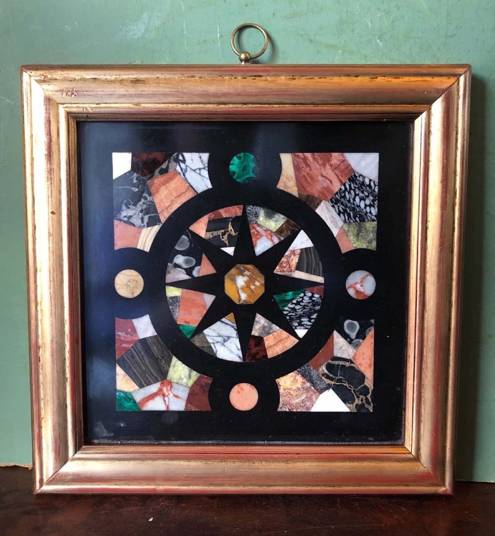 A square 19th-century Ashford black marble panel inlaid with colourful specimen marble geometric shapes forming a central star motif, set within a gilt wood frame with a top brass hanging ring. View II