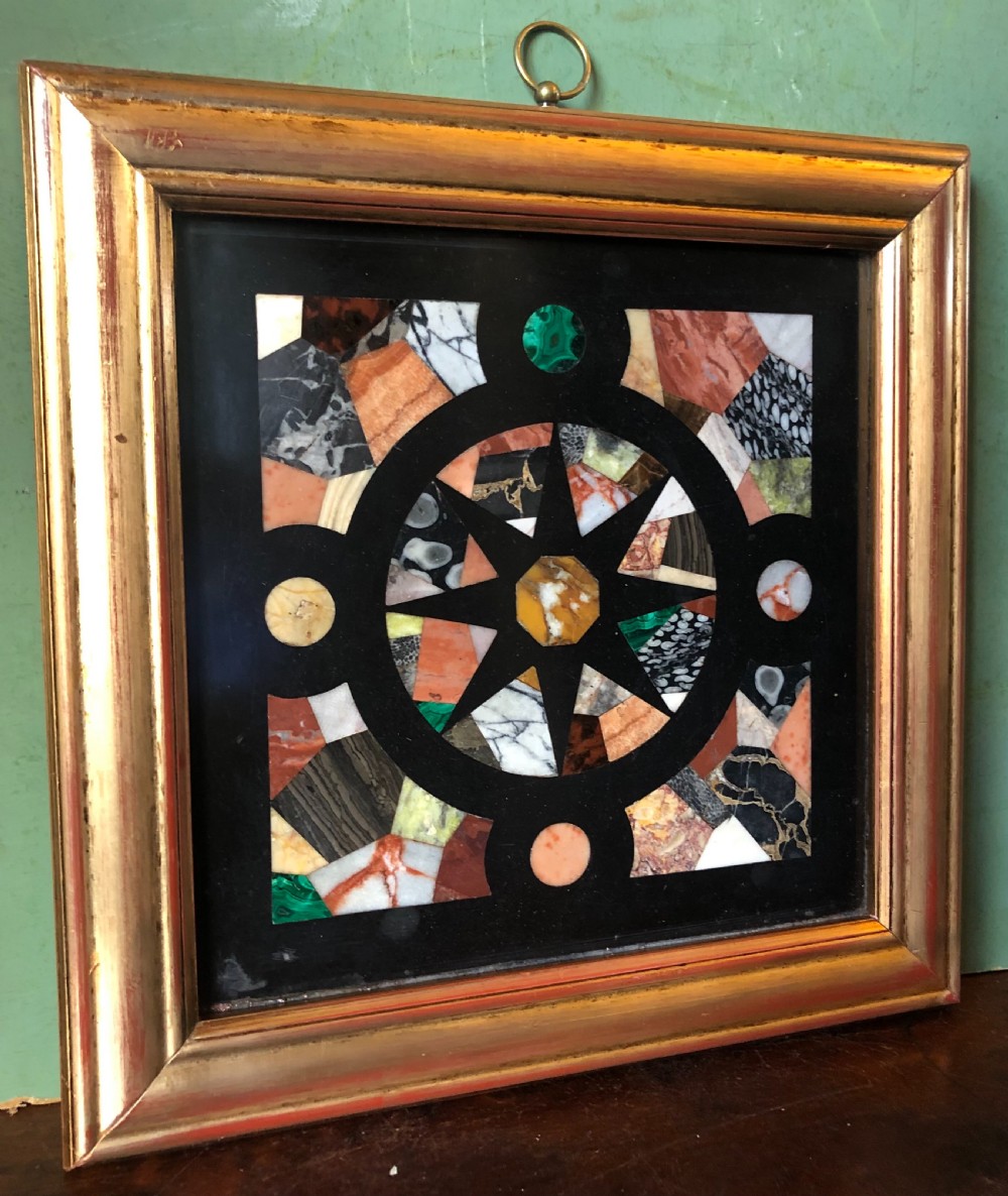 A square 19th-century Ashford black marble panel inlaid with colourful specimen marble geometric shapes forming a central star motif, set within a gilt wood frame with a top brass hanging ring. View V