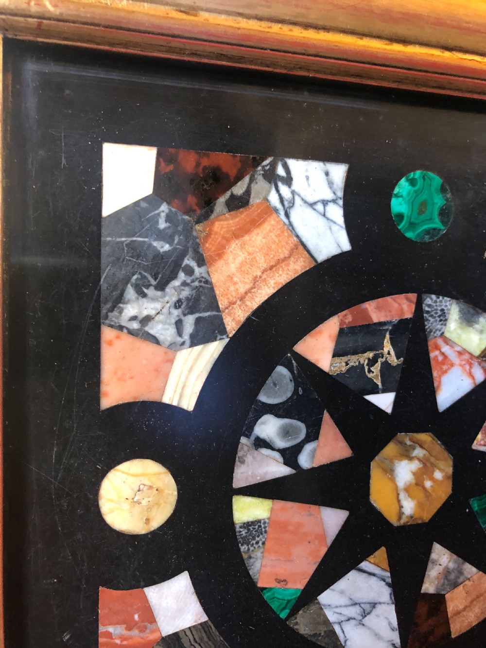 A square 19th-century Ashford black marble panel inlaid with colourful specimen marble geometric shapes forming a central star motif, set within a gilt wood frame with a top brass hanging ring. View VI