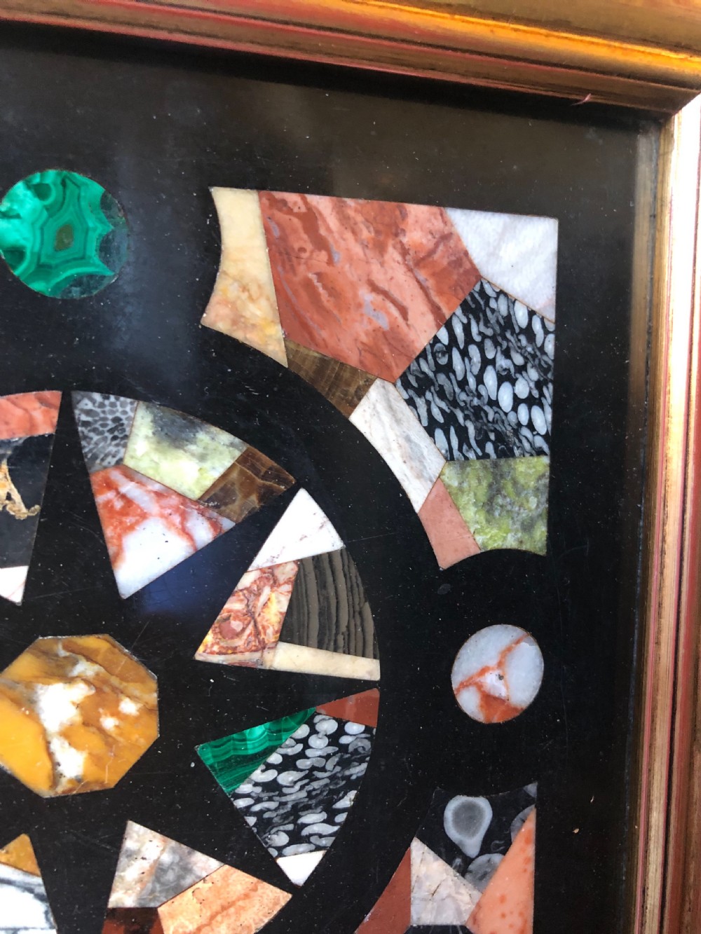 A square 19th-century Ashford black marble panel inlaid with colourful specimen marble geometric shapes forming a central star motif, set within a gilt wood frame with a top brass hanging ring. View VII