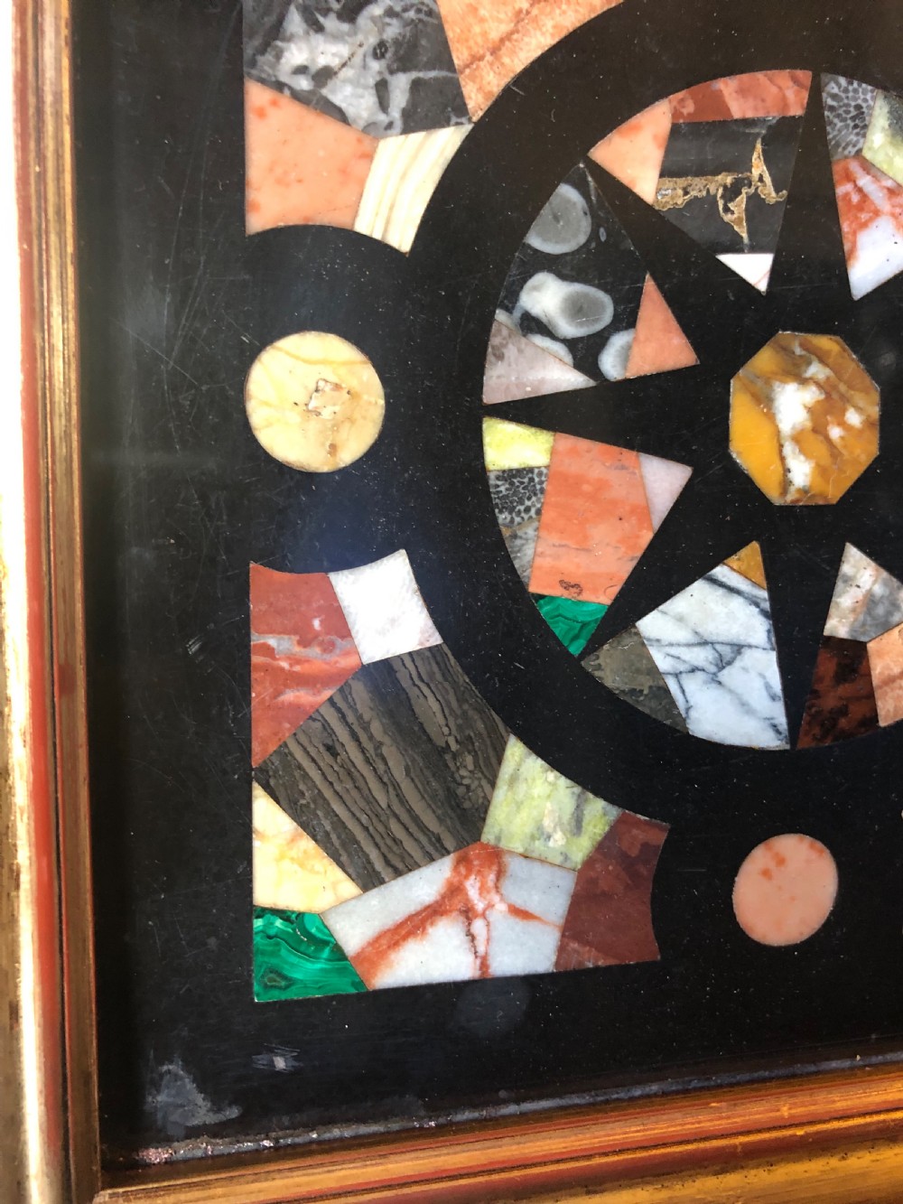 A square 19th-century Ashford black marble panel inlaid with colourful specimen marble geometric shapes forming a central star motif, set within a gilt wood frame with a top brass hanging ring. View VIII
