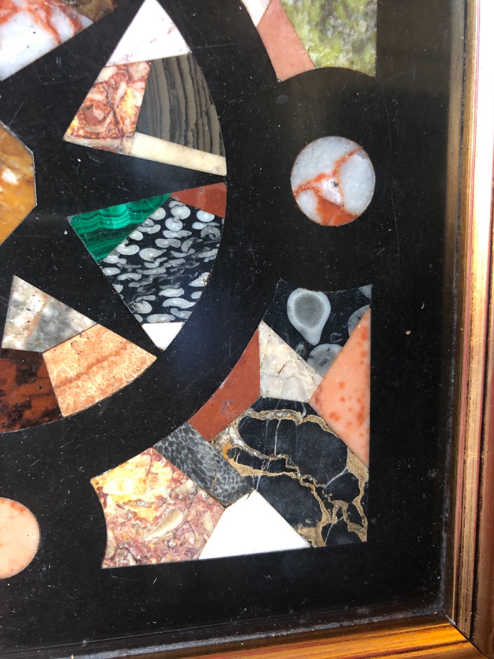 A square 19th-century Ashford black marble panel inlaid with colourful specimen marble geometric shapes forming a central star motif, set within a gilt wood frame with a top brass hanging ring. View IX