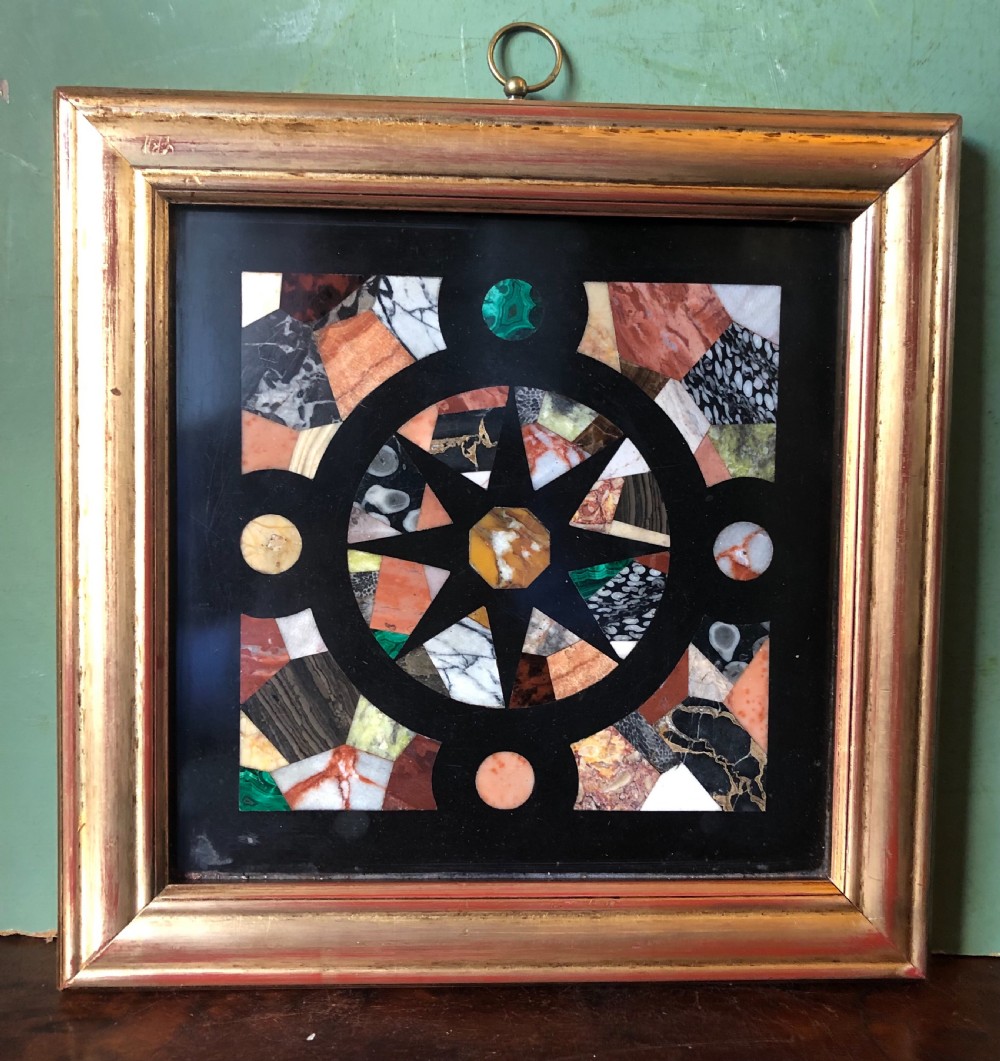 A square 19th-century Ashford black marble panel inlaid with colourful specimen marble geometric shapes forming a central star motif, set within a gilt wood frame with a top brass hanging ring. View X