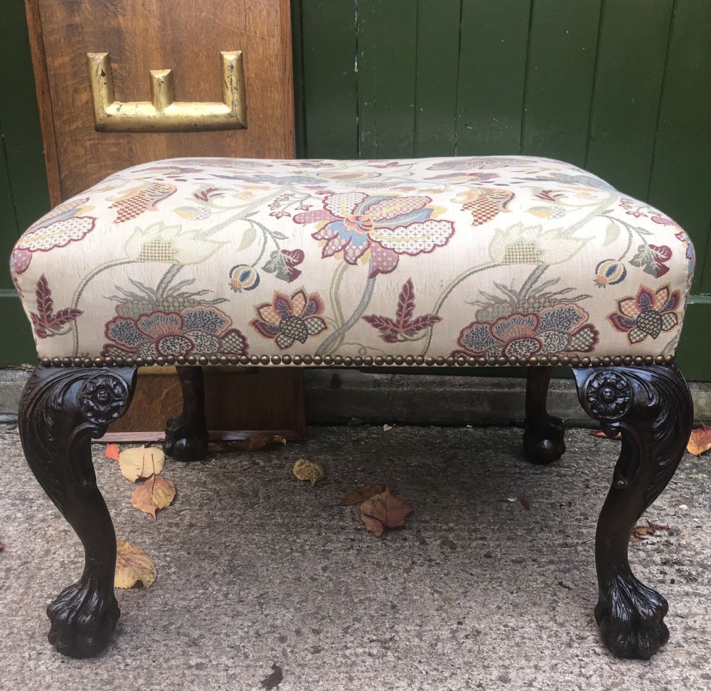 A rectangular floral upholstered stool featuring dark carved walnut cabriole legs with floral knees and claw-and-ball feet.