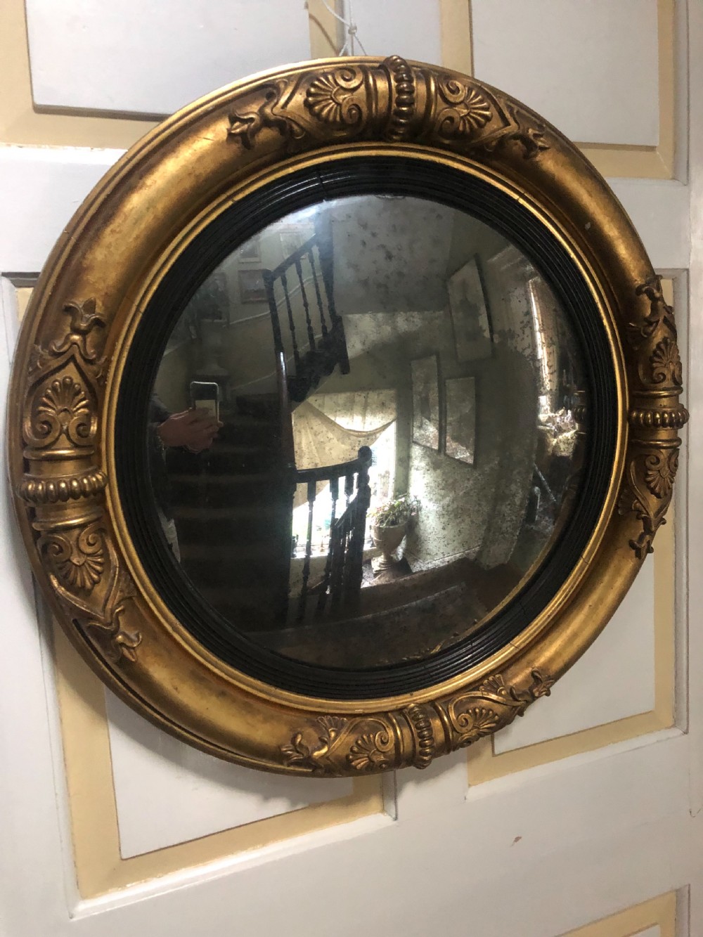 Early 19th-century circular Regency giltwood convex wall mirror decorated with anthemion leaf carvings and an ebonised reeded inner slip.
