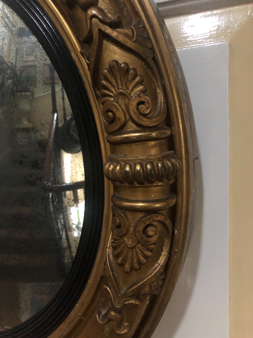 Early 19th-century circular Regency giltwood convex wall mirror decorated with anthemion leaf carvings and an ebonised reeded inner slip. View II