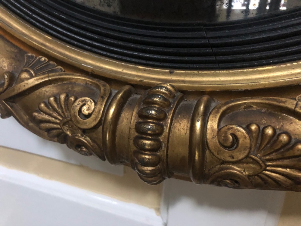 Early 19th-century circular Regency giltwood convex wall mirror decorated with anthemion leaf carvings and an ebonised reeded inner slip. View VIII