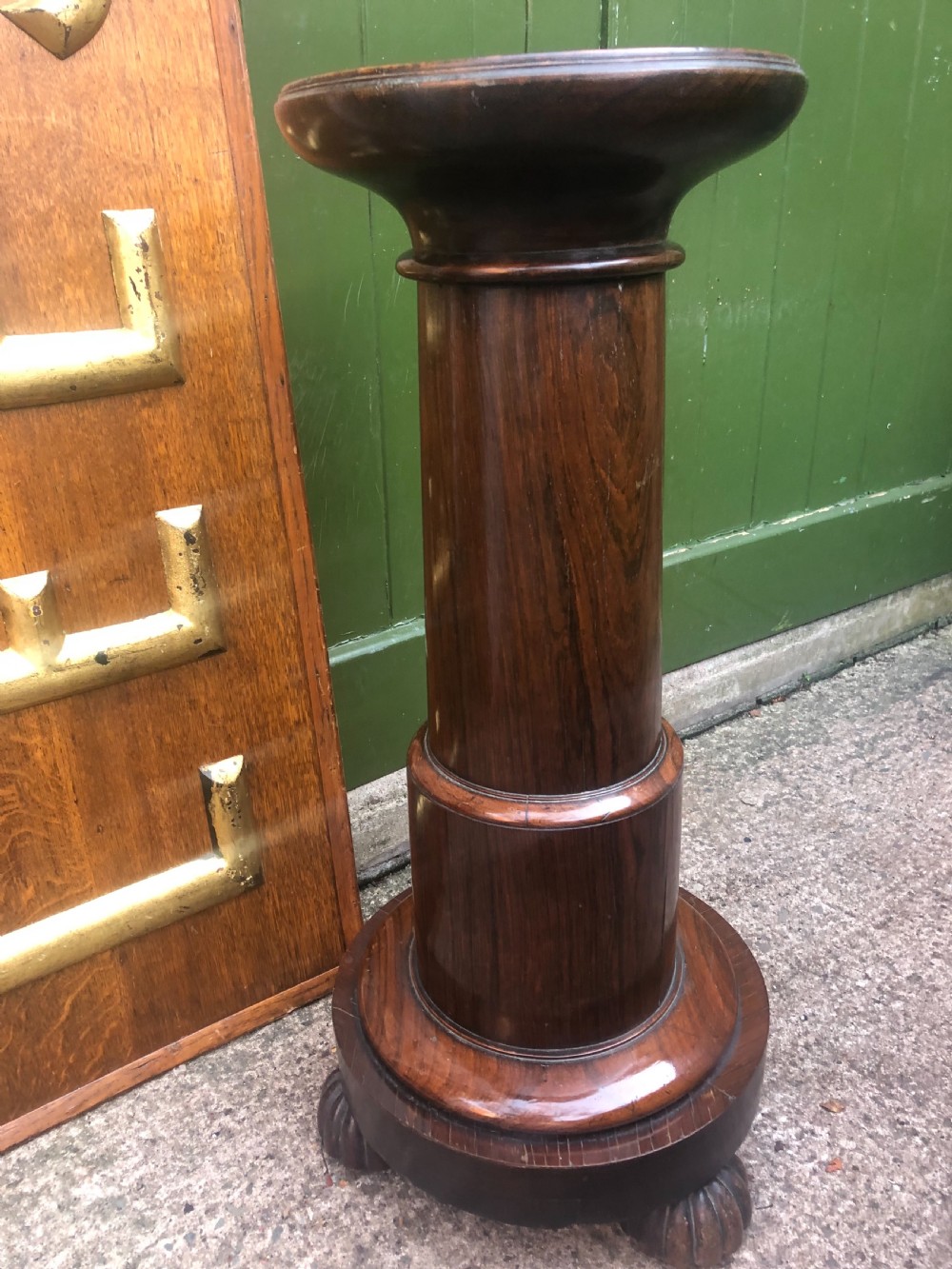 A dark brown turned rosewood columnar sculpture pedestal featuring a moulded top disc, architectural cylindrical shaft, and carved feet. View II