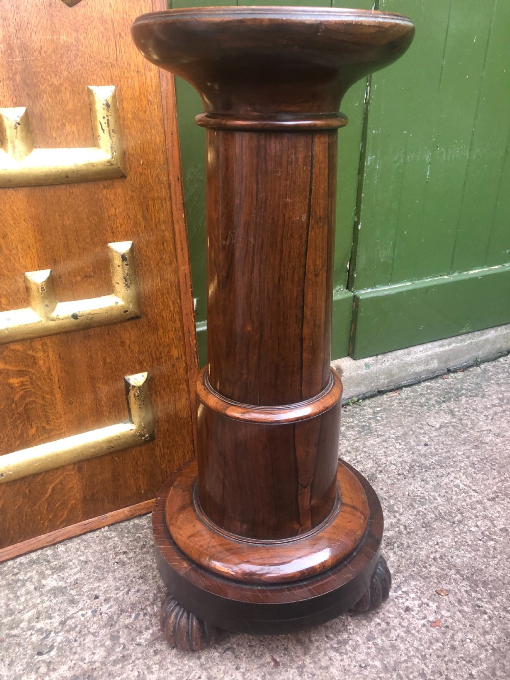 A dark brown turned rosewood columnar sculpture pedestal featuring a moulded top disc, architectural cylindrical shaft, and carved feet. View VII
