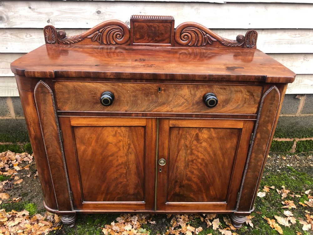 An early 19th-century William IV mahogany serving buffet featuring a carved scroll upstand, a top drawer with turned knobs, and twin panelled cupboard doors. View II