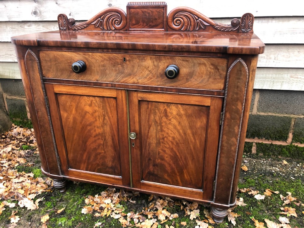 An early 19th-century William IV mahogany serving buffet featuring a carved scroll upstand, a top drawer with turned knobs, and twin panelled cupboard doors. View III
