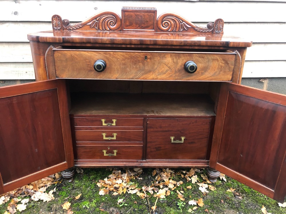 An early 19th-century William IV mahogany serving buffet featuring a carved scroll upstand, a top drawer with turned knobs, and twin panelled cupboard doors. View V