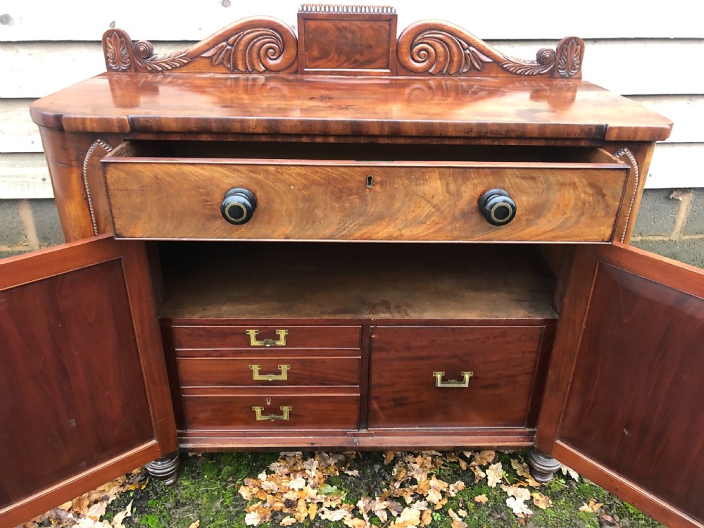 An early 19th-century William IV mahogany serving buffet featuring a carved scroll upstand, a top drawer with turned knobs, and twin panelled cupboard doors. View VIII