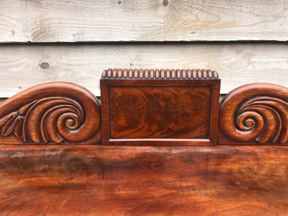 An early 19th-century William IV mahogany serving buffet featuring a carved scroll upstand, a top drawer with turned knobs, and twin panelled cupboard doors. View IX