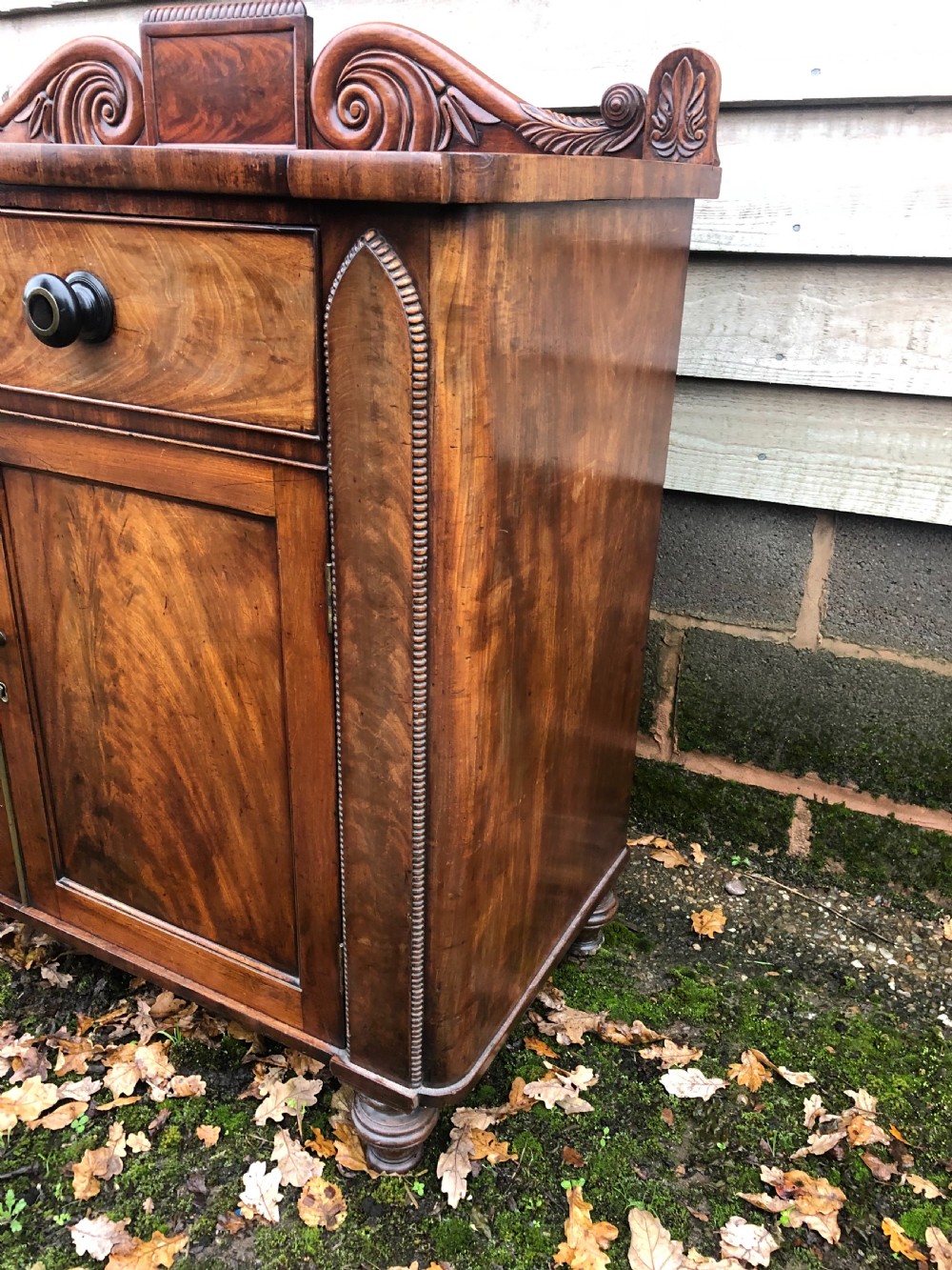 An early 19th-century William IV mahogany serving buffet featuring a carved scroll upstand, a top drawer with turned knobs, and twin panelled cupboard doors. View XIII
