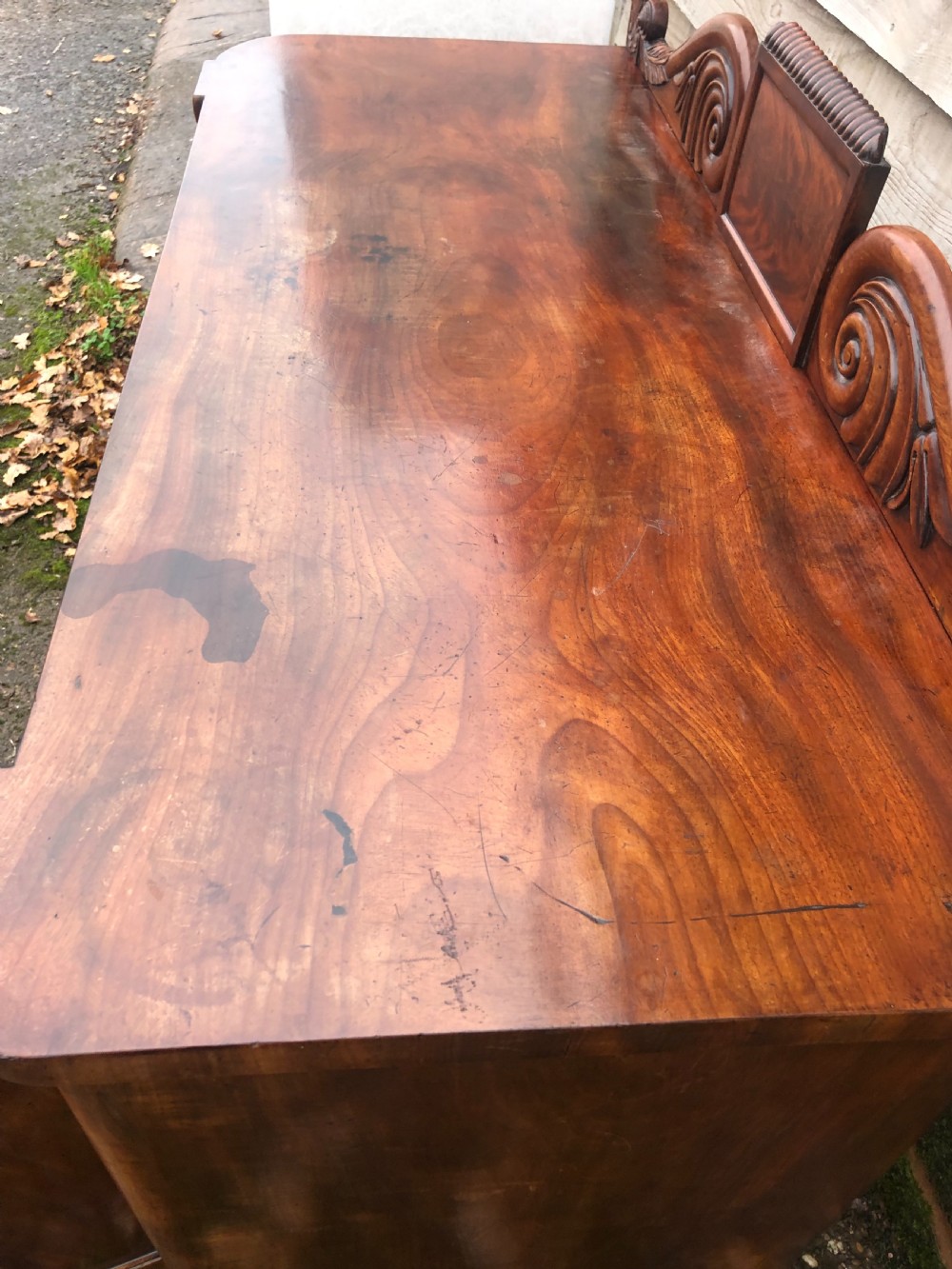 An early 19th-century William IV mahogany serving buffet featuring a carved scroll upstand, a top drawer with turned knobs, and twin panelled cupboard doors. View XIV