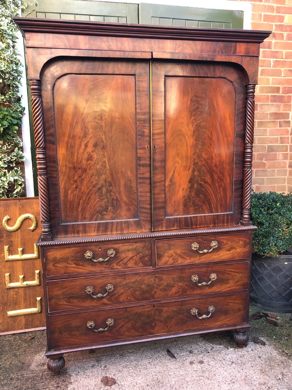 A William IV flame mahogany linen press featuring a double door upper cupboard with rope-twist side columns set above a lower chest of drawers with brass handles. View II