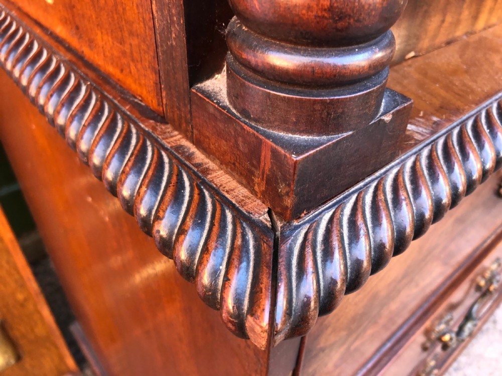 A William IV flame mahogany linen press featuring a double door upper cupboard with rope-twist side columns set above a lower chest of drawers with brass handles. View III