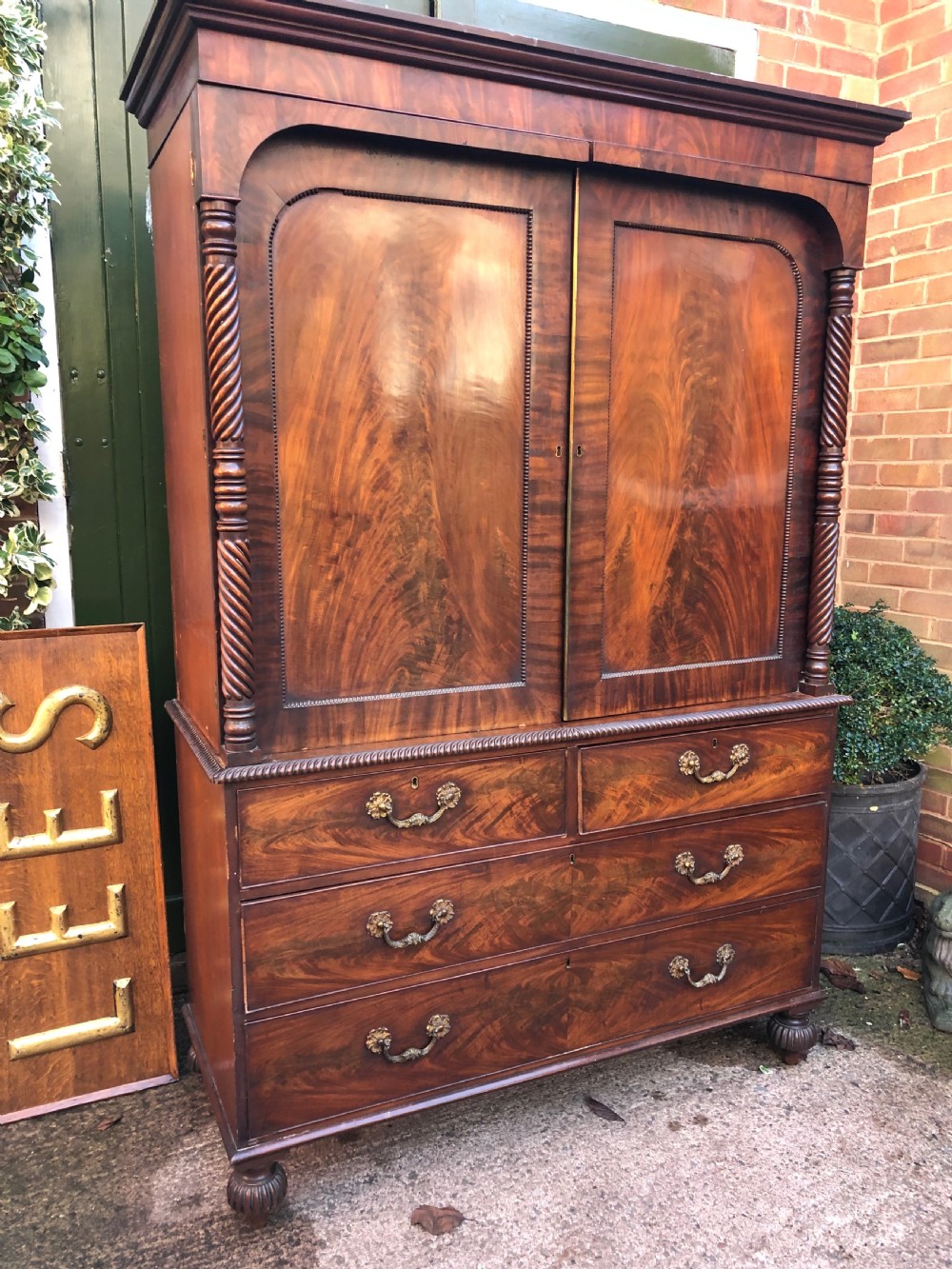 A William IV flame mahogany linen press featuring a double door upper cupboard with rope-twist side columns set above a lower chest of drawers with brass handles. View VI