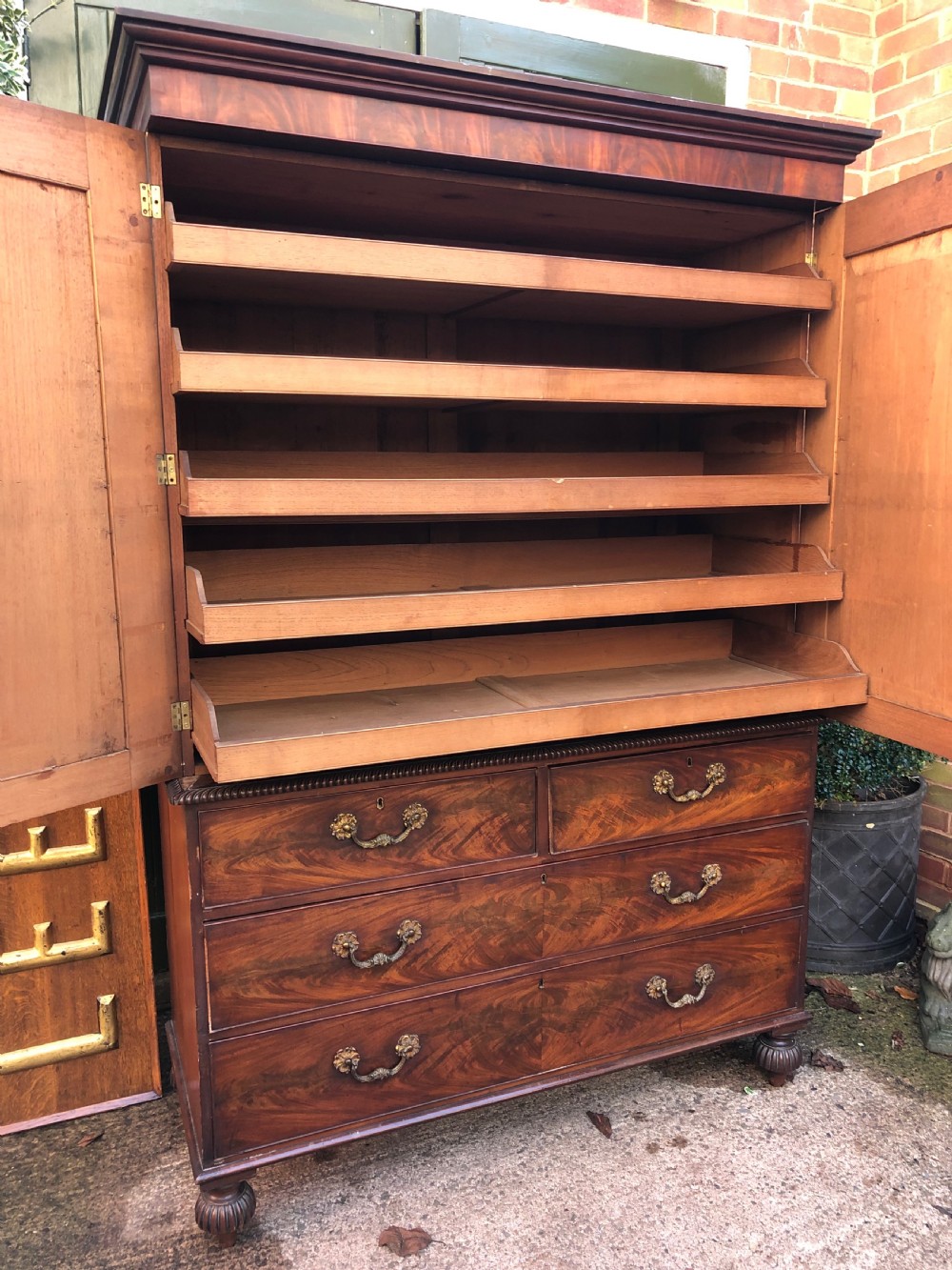 A William IV flame mahogany linen press featuring a double door upper cupboard with rope-twist side columns set above a lower chest of drawers with brass handles. View IX