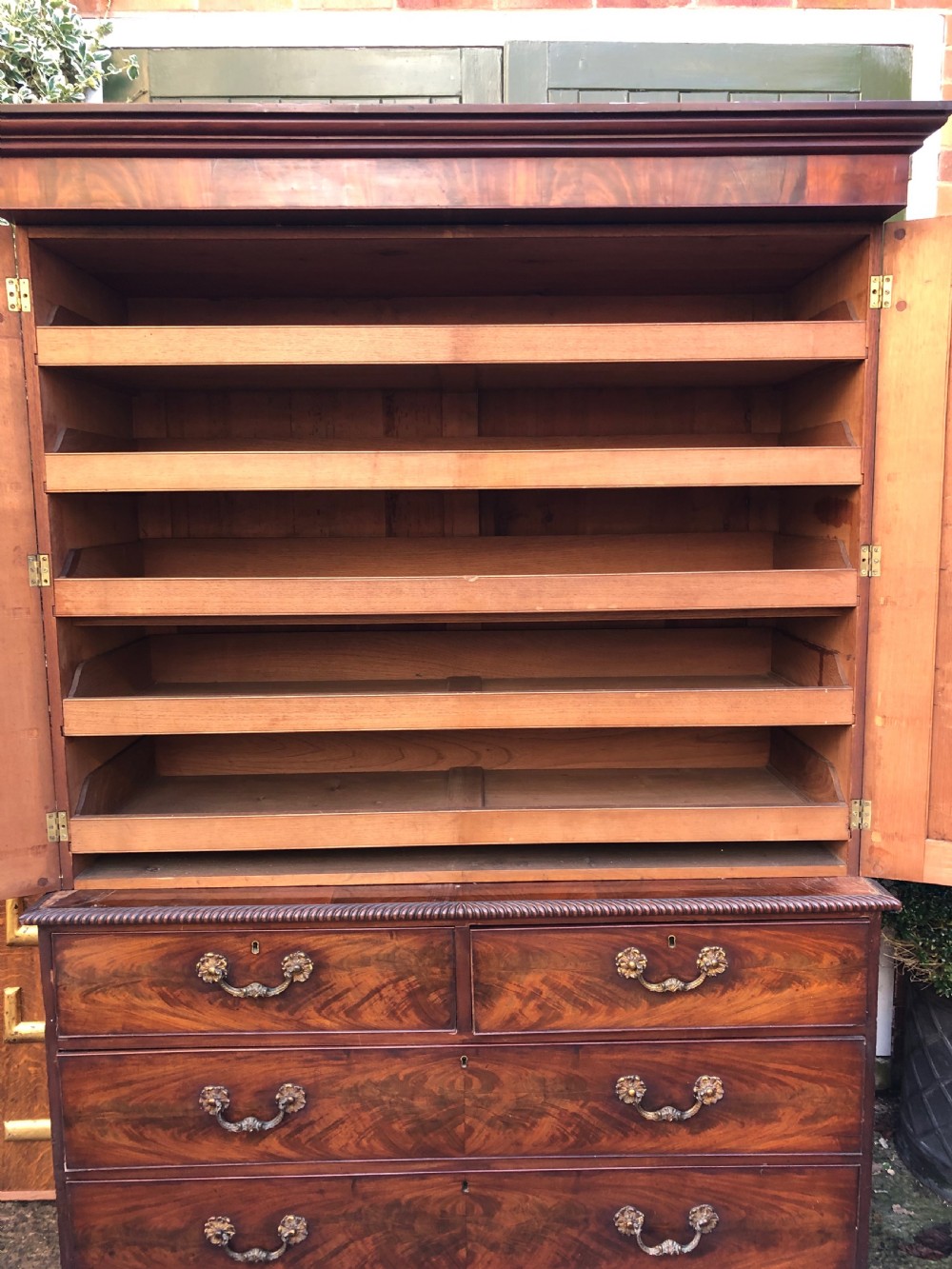 A William IV flame mahogany linen press featuring a double door upper cupboard with rope-twist side columns set above a lower chest of drawers with brass handles. View X