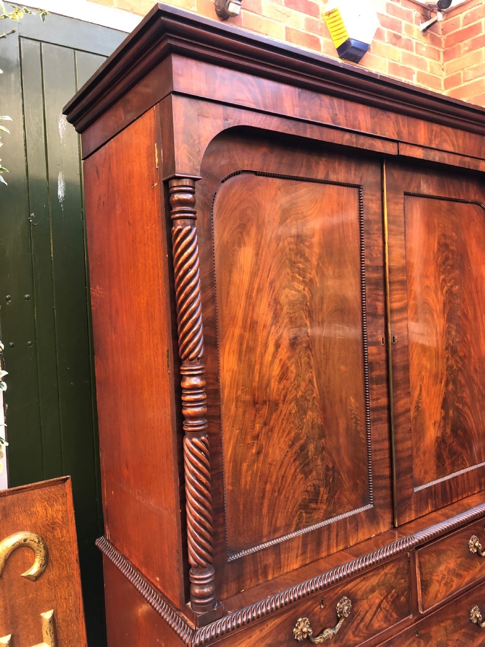 A William IV flame mahogany linen press featuring a double door upper cupboard with rope-twist side columns set above a lower chest of drawers with brass handles. View XI