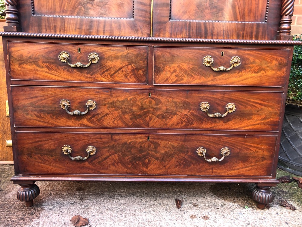 A William IV flame mahogany linen press featuring a double door upper cupboard with rope-twist side columns set above a lower chest of drawers with brass handles. View XIV