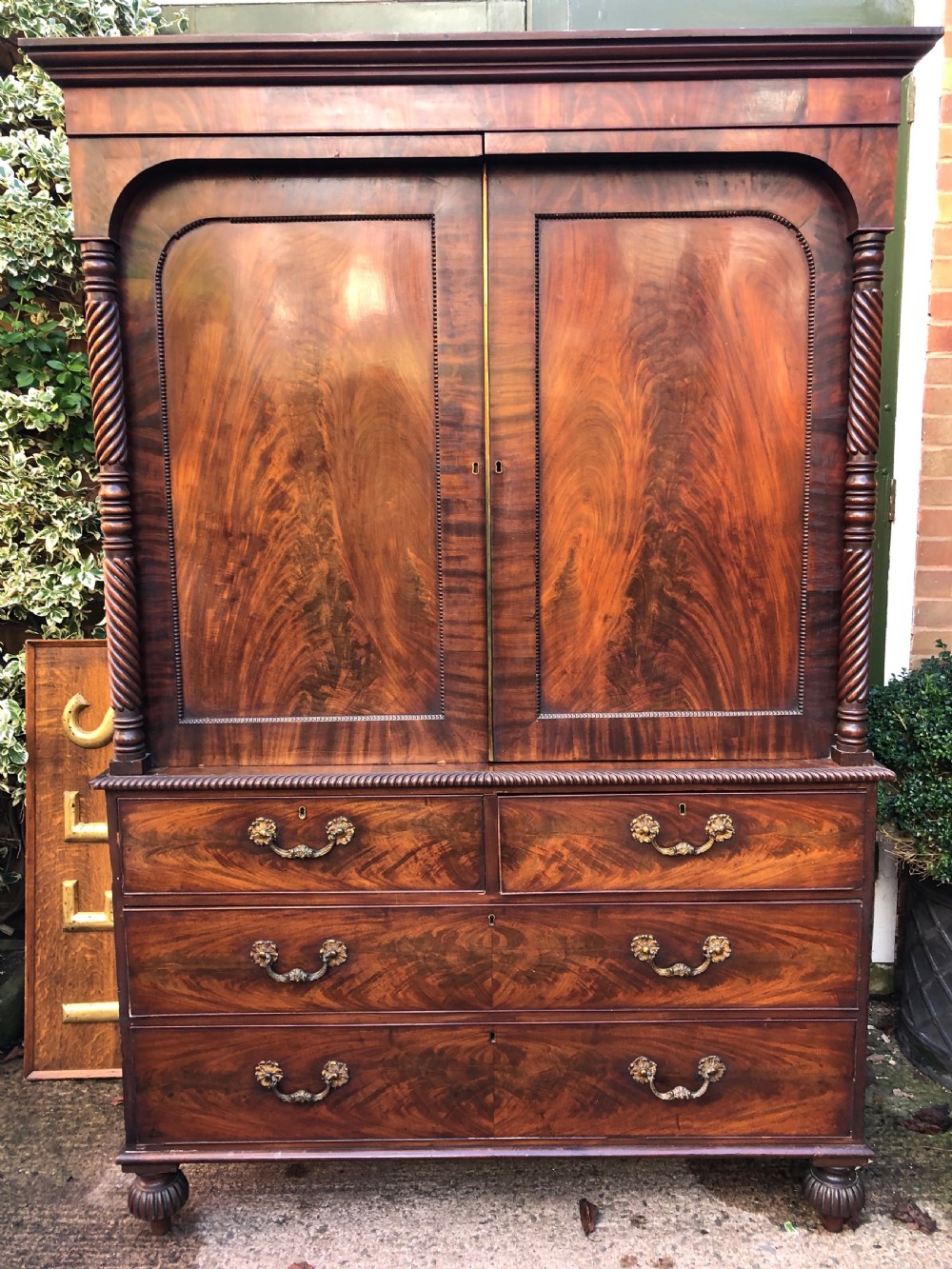A William IV flame mahogany linen press featuring a double door upper cupboard with rope-twist side columns set above a lower chest of drawers with brass handles. View XVI