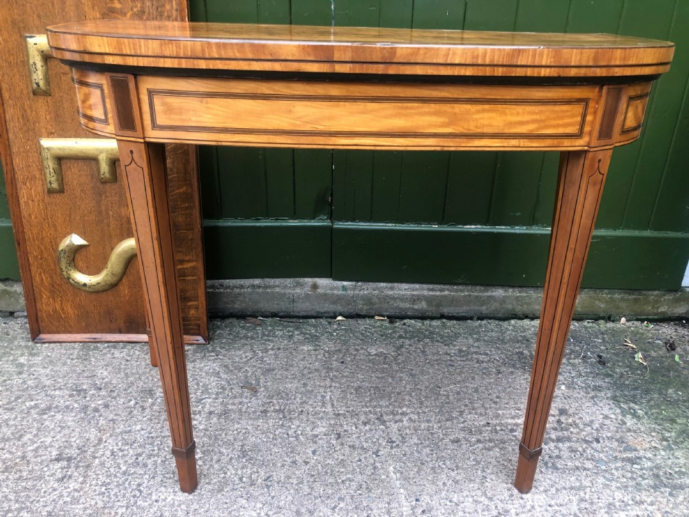 A late 18th-century George III satinwood fold-over card table featuring rosewood crossbanding, line inlay, and tapered square legs.