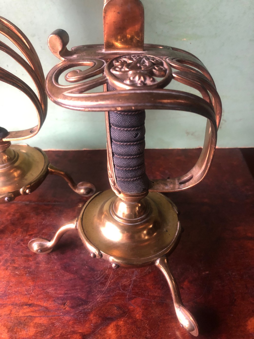 A pair of late nineteenth-century gilded brass candlelamps modelled as cavalry dress swords with basket guards, standing on tripod feet with conical shades. View III