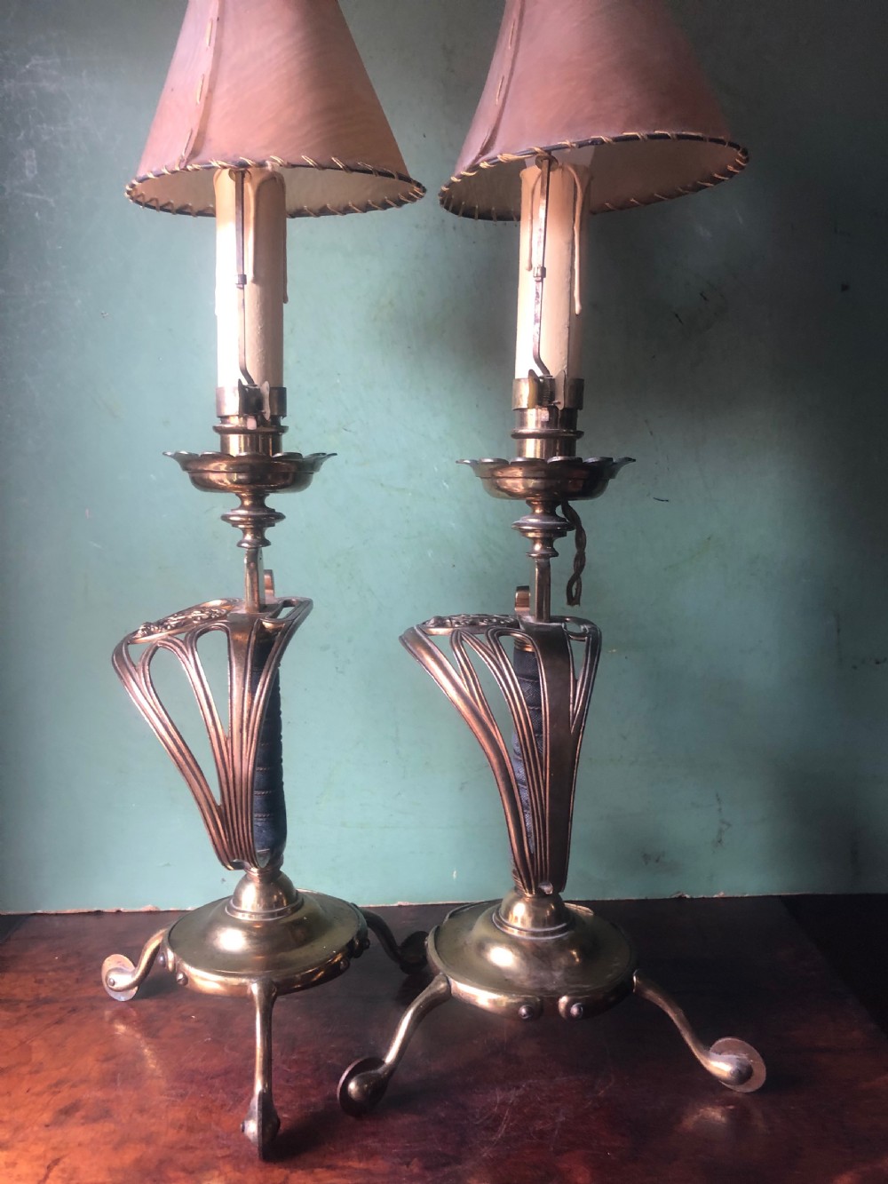 A pair of late nineteenth-century gilded brass candlelamps modelled as cavalry dress swords with basket guards, standing on tripod feet with conical shades. View V