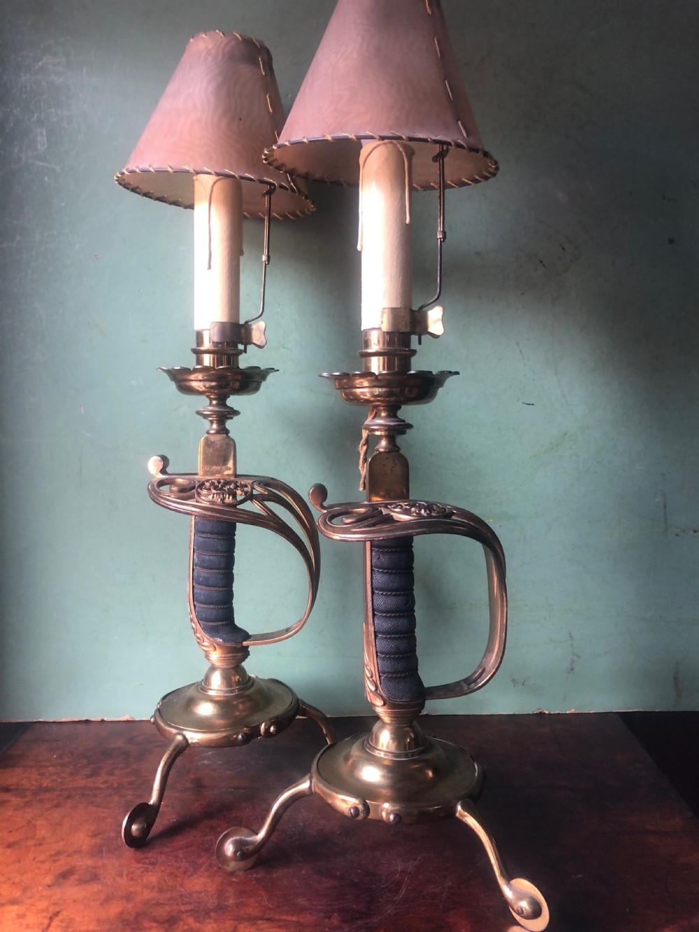 A pair of late nineteenth-century gilded brass candlelamps modelled as cavalry dress swords with basket guards, standing on tripod feet with conical shades. View VII