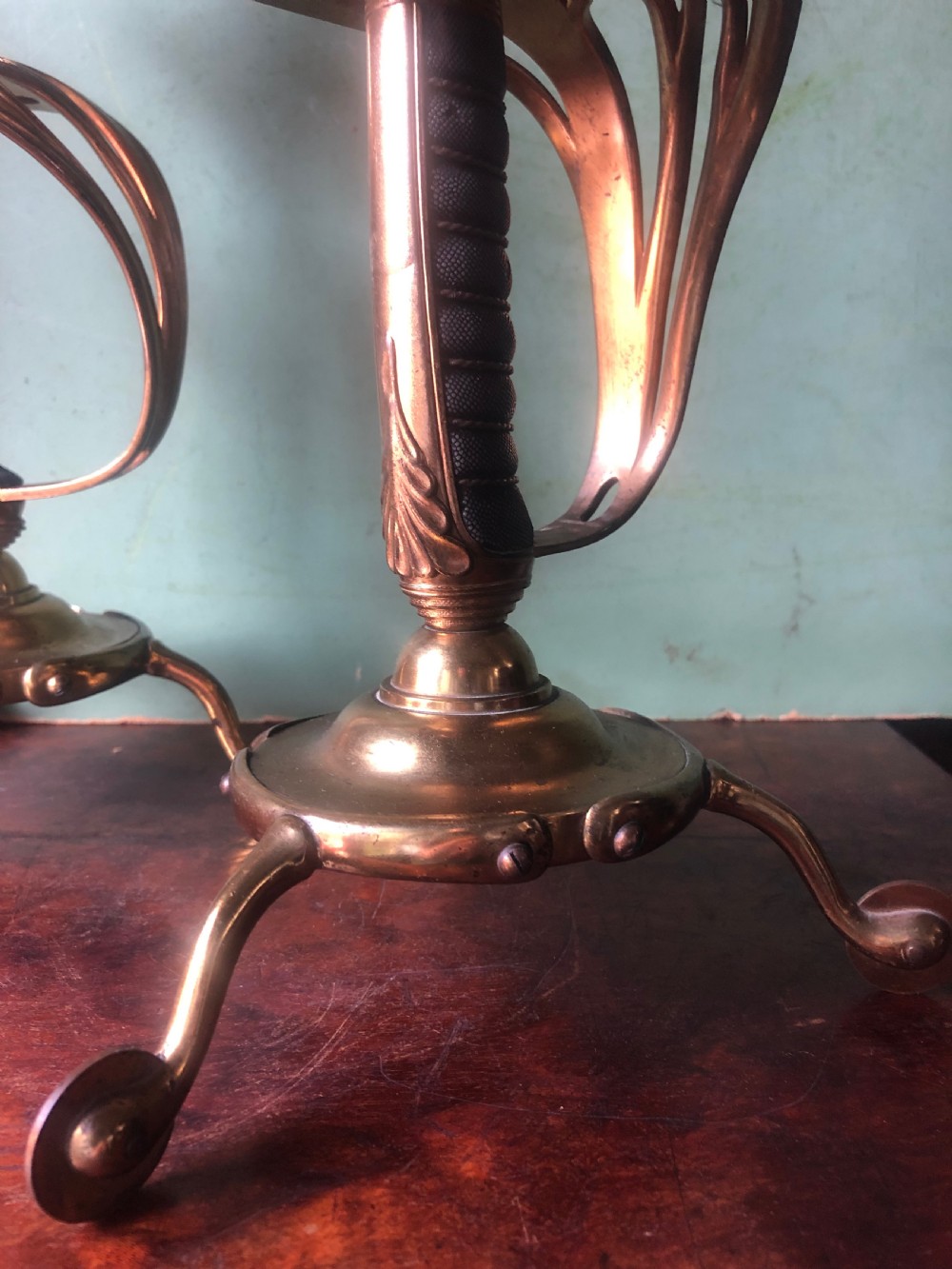 A pair of late nineteenth-century gilded brass candlelamps modelled as cavalry dress swords with basket guards, standing on tripod feet with conical shades. View IX