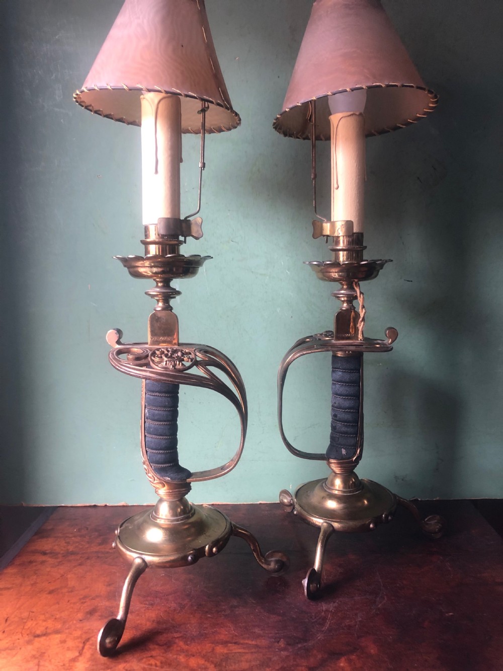 A pair of late nineteenth-century gilded brass candlelamps modelled as cavalry dress swords with basket guards, standing on tripod feet with conical shades. View X