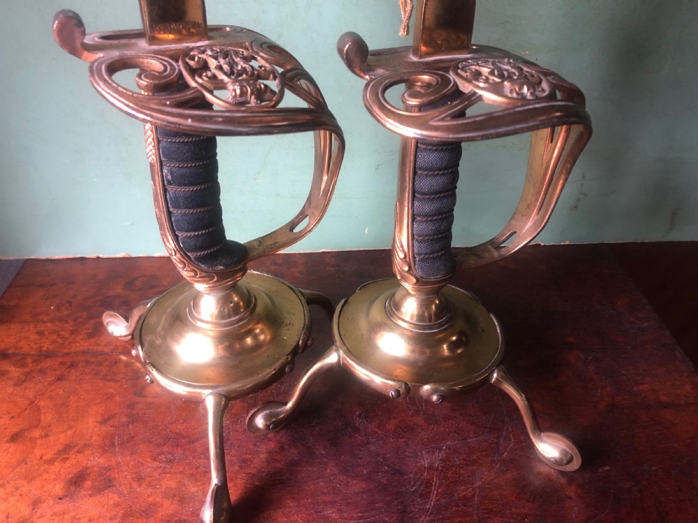 A pair of late nineteenth-century gilded brass candlelamps modelled as cavalry dress swords with basket guards, standing on tripod feet with conical shades. View XI