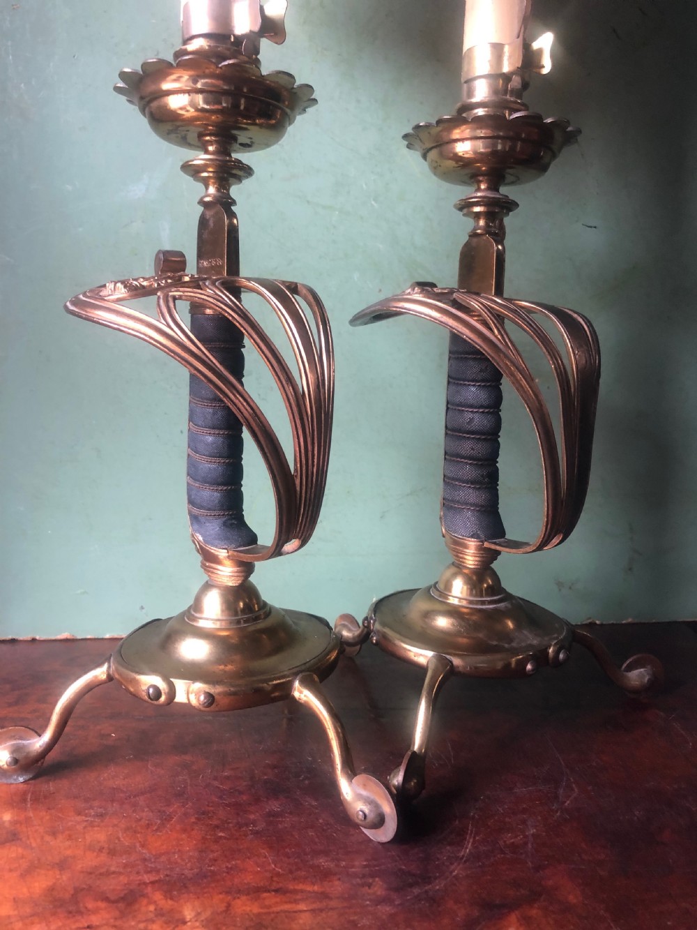 A pair of late nineteenth-century gilded brass candlelamps modelled as cavalry dress swords with basket guards, standing on tripod feet with conical shades. View XII