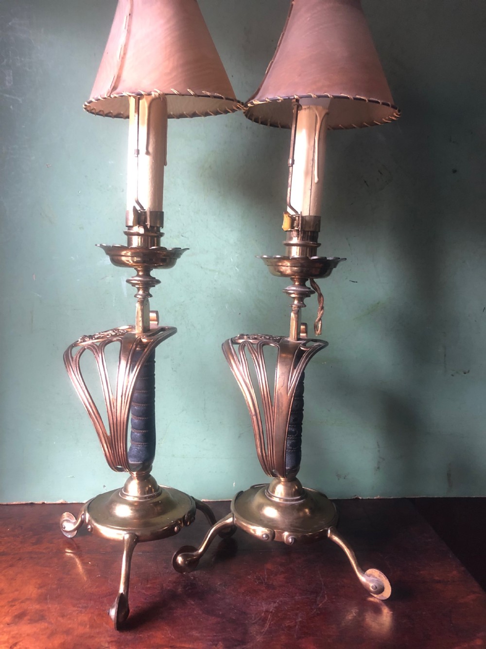 A pair of late nineteenth-century gilded brass candlelamps modelled as cavalry dress swords with basket guards, standing on tripod feet with conical shades. View XIV