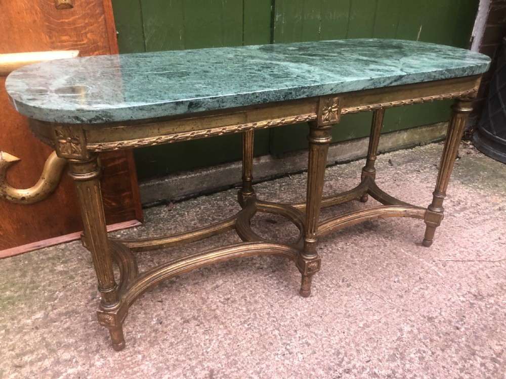 An early 20th-century French Louis XVI style low table with a green marble top, giltwood frame, fluted legs, and carved rosette details.