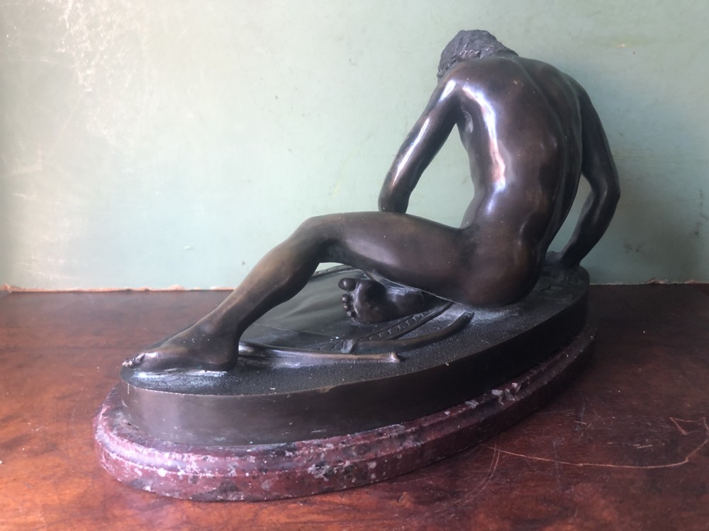 A late 19th-century dark bronze sculpture depicting a recumbent classical warrior mounted on an oval red marble base. View X