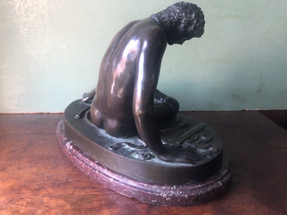 A late 19th-century dark bronze sculpture depicting a recumbent classical warrior mounted on an oval red marble base. View XI