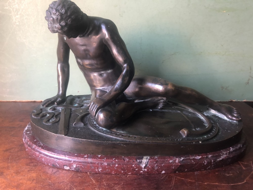 A late 19th-century dark bronze sculpture depicting a recumbent classical warrior mounted on an oval red marble base. View XII