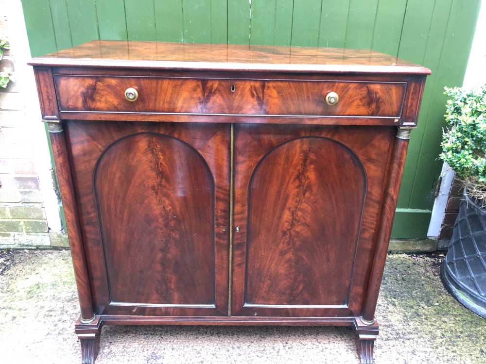 An early nineteenth-century flame mahogany side cabinet with arch-panelled double doors, top drawer, and brass fittings. View II